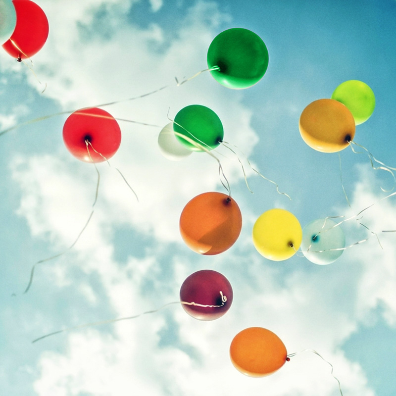 Ballons de couleur s'envolant librement dans un ciel bleu nuageux, symbolisant le lâcher-prise au quotidien